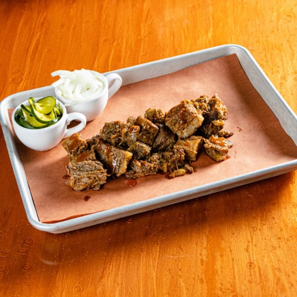 Reunion BBQ's burnt ends, with sliced pickles and onions, on a metal tray with butcher paper.