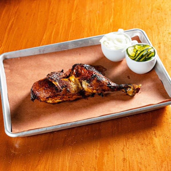 Reunion BBQ's smoked chicken with sides of sliced onions and pickled cucumbers on a metal tray.