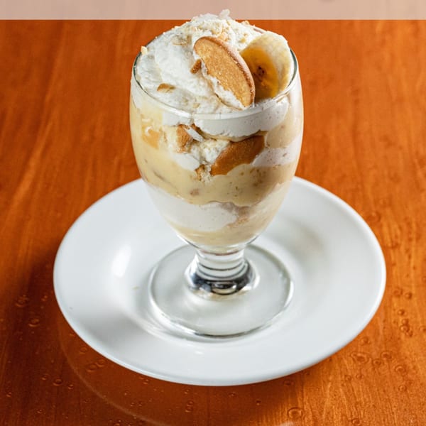 Banana pudding dessert in a glass with whipped cream, vanilla wafers, and banana slices.