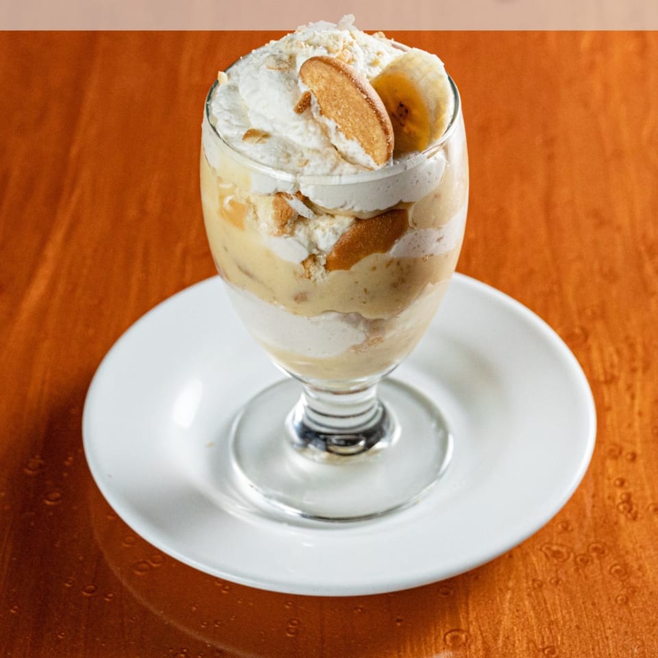 Banana pudding dessert in a glass with whipped cream, vanilla wafers, and banana slices.