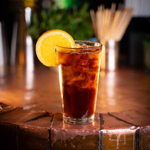 Reunion BBQ's dark iced tea with an orange slice, on a rustic copper bar.