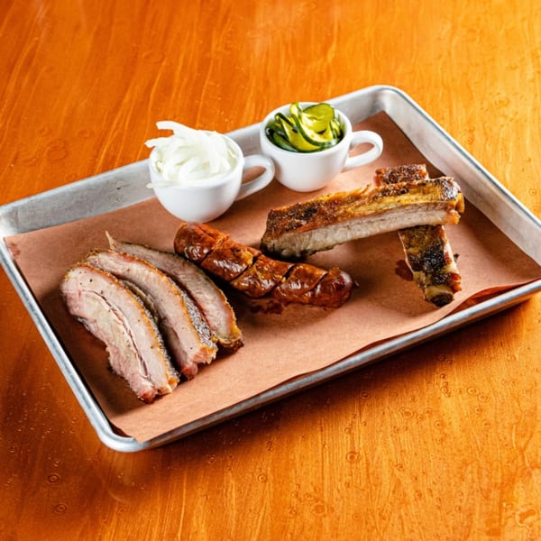 Reunion BBQ platter with sliced brisket, sausage, ribs, onions, and pickles on a metal tray.