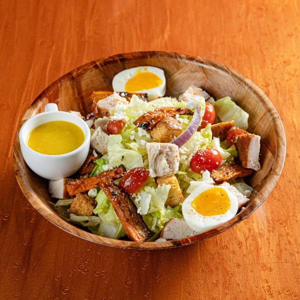 Reunion BBQ's Cobb salad with chicken, bacon, eggs, tomatoes, and dressing in a wooden bowl.