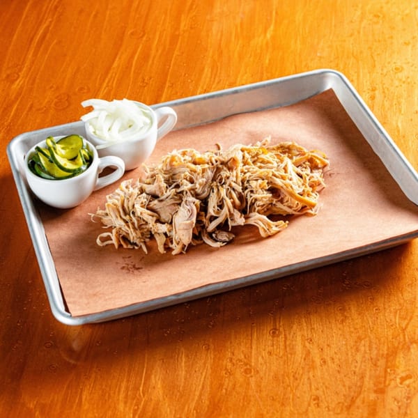 Reunion BBQ pulled pork on a tray with sliced pickles and onions in white ramekins.