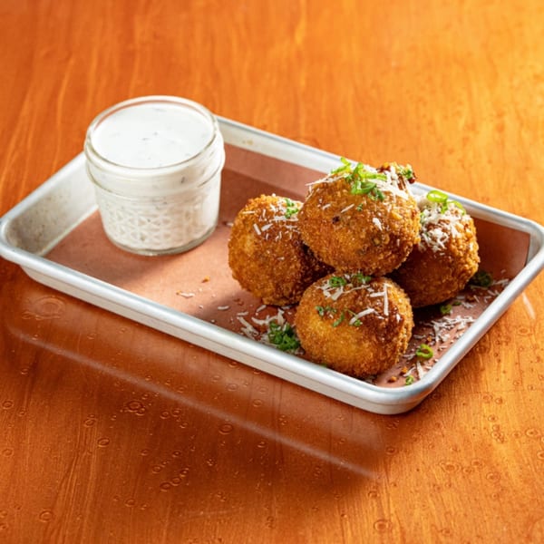 Four golden-brown fried balls, garnished with cheese and chives, served with a side of ranch dressing.