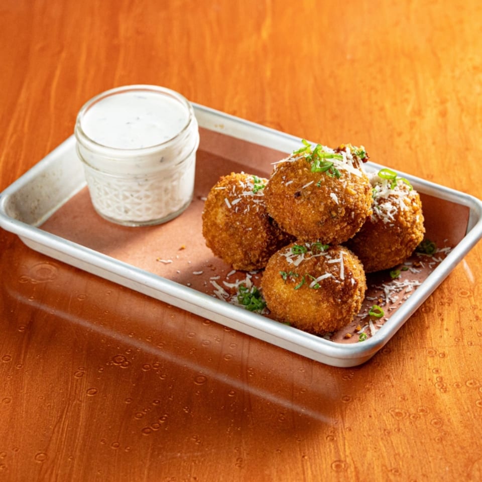 Four golden-brown fried balls, garnished with cheese and chives, served with a side of ranch dressing.